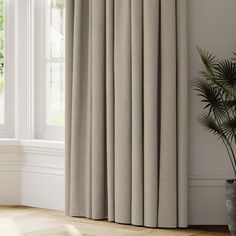 an open window with curtains and a potted plant in front of it on the floor