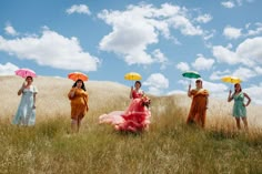 four women in dresses and umbrellas standing in a field