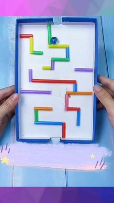 two hands are holding up a plastic board that has colored sticks in the shape of a maze