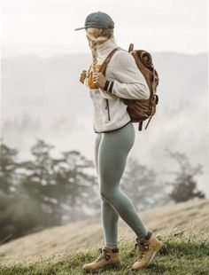 a woman in tights and a hat standing on top of a grass covered hill