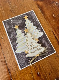 a merry christmas card on a wooden table with gold foil stars and a small tree