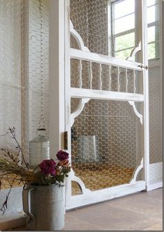 a vase filled with flowers sitting next to an open door that has chicken wire on it