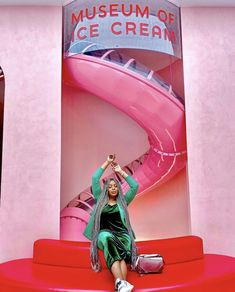 a woman sitting on top of a red bench in front of a pink wall with an ice cream sign