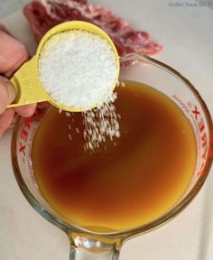 a person pouring sugar into a glass bowl filled with liquid on top of a table