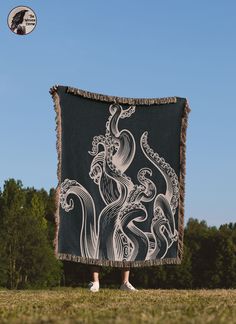 a person standing in the grass holding up a black and white blanket with an octopus on it