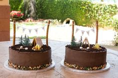 two cakes sitting on top of a table covered in chocolate frosting and decorated with decorations