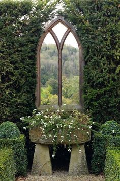 a stone bench sitting in front of a large window surrounded by bushes and shrubbery