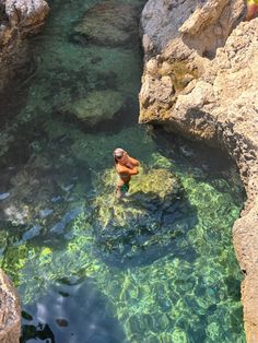 a man is swimming in the clear blue water near some rocks and boulders, with green algae growing on them