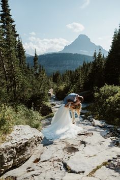 a bride and groom are kissing on the rocks in the woods with mountains in the background