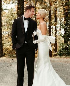 a man and woman in formal wear standing next to each other on a road surrounded by trees