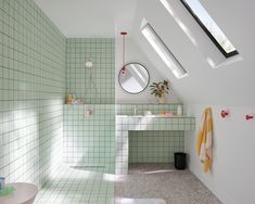 an attic bathroom with green tile and white walls, along with a skylight above the bathtub