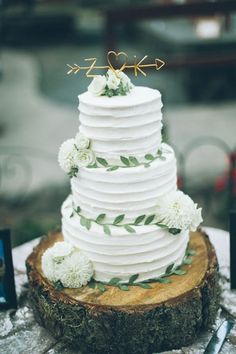 a white wedding cake sitting on top of a wooden slice