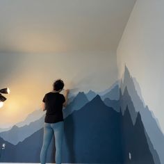 a woman painting a mountain scene on the wall in a room with mountains painted on it