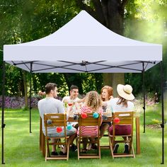 a group of people sitting around a wooden table under a white tent in the grass