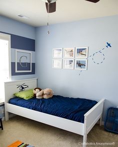 a bedroom with blue walls and pictures on the wall above the bed, along with a teddy bear