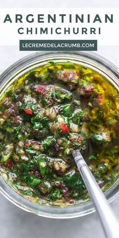 a glass bowl filled with greens and meats next to a spoon on top of a table