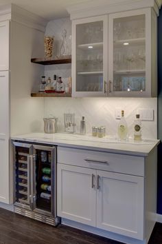 a kitchen with white cabinets and wine glasses on the counter top, next to an open refrigerator