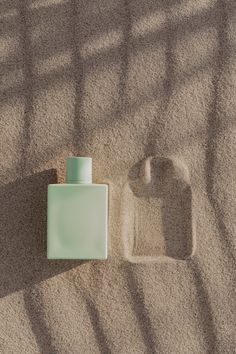 an empty bottle sitting on top of sand next to a small square shaped soap dispenser