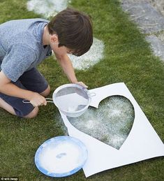 a young boy is making a heart out of paper on the grass with a grater