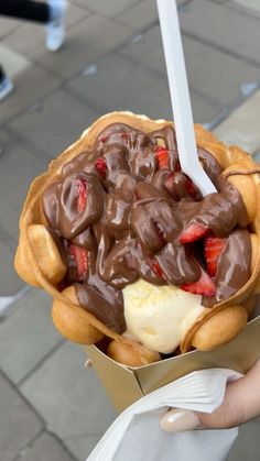 a person holding a waffle with chocolate and strawberries in it on the street