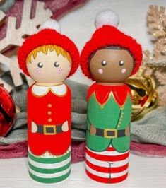 two wooden dolls sitting next to each other on top of a white table covered in christmas decorations