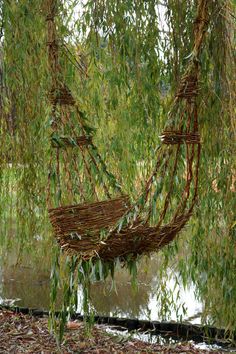 a wicker hammock hanging from a willow tree in front of a river