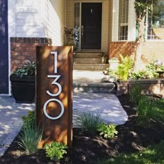 a house number sign sitting in front of a door with plants and flowers around it