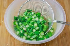 a white bowl filled with green vegetables on top of a wooden table next to a metal strainer