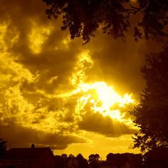 the sun is setting behind some clouds in the sky over houses and trees on a cloudy day