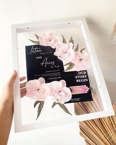 a person holding up a white frame with pink flowers on it