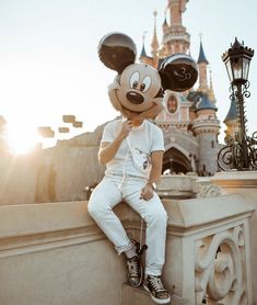 a person sitting on top of a stone wall next to a mickey mouse head in front of a castle