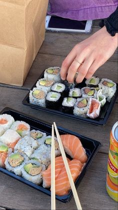 two black trays filled with sushi and chopsticks next to a can of soda