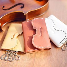 three leather wallets sitting on top of a wooden table next to a violin and keychain