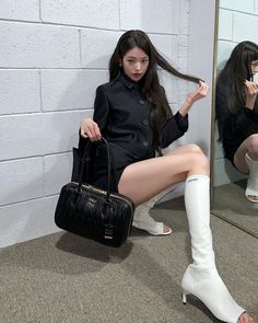 a woman sitting in front of a mirror holding a black purse and wearing white boots