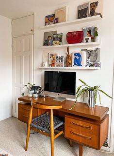 a desk with a computer on top of it in front of a wall mounted shelf