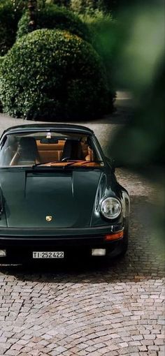 a green sports car parked on the side of a road next to bushes and trees