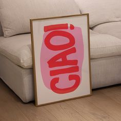 a framed poster sitting on the floor in front of a white couch with red lettering