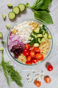 a bowl filled with pasta, tomatoes, cucumbers and other veggies