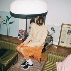 a woman sitting on top of a green couch in a living room next to a lamp