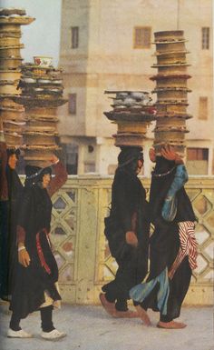 three people walking down the street with stacks of books on their heads