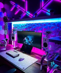 a desk with a computer, keyboard and speakers in front of a purple wall decorated with geometric shapes