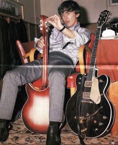 a young man sitting in a chair with two guitars on the floor next to him