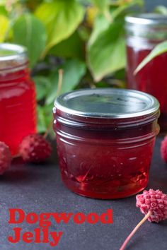 two jars filled with raspberry jelly sitting on top of a table next to flowers