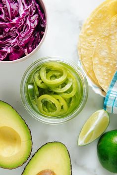 an avocado, cabbage and sliced limes on a marble counter top with tortillas