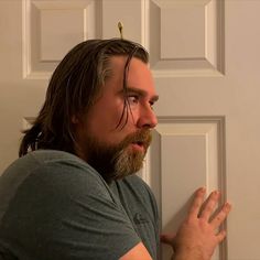 a man with long hair and a beard standing in front of a door holding his hands out