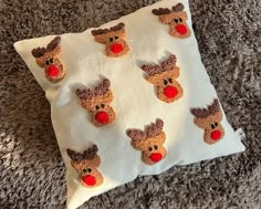 a white pillow with brown and red knitted reindeer faces on it sitting on carpet