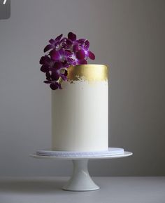 a white and gold cake with purple flowers on top