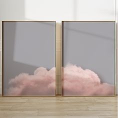 two framed pictures with pink clouds in the sky behind them on a wooden floor next to a white wall