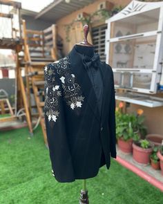 a black jacket with white flowers on it sitting on top of a green lawn next to potted plants