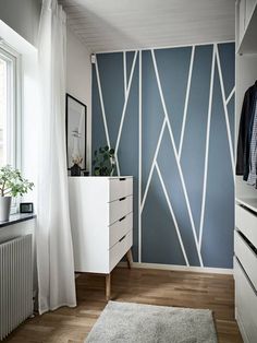 a bedroom with blue and white wallpaper next to a dresser in front of a window